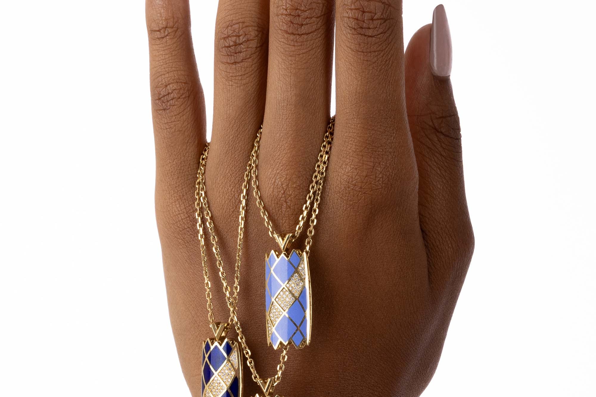 Three Castle Necklaces in light blue, dark blue, and red are draped over a model’s hand