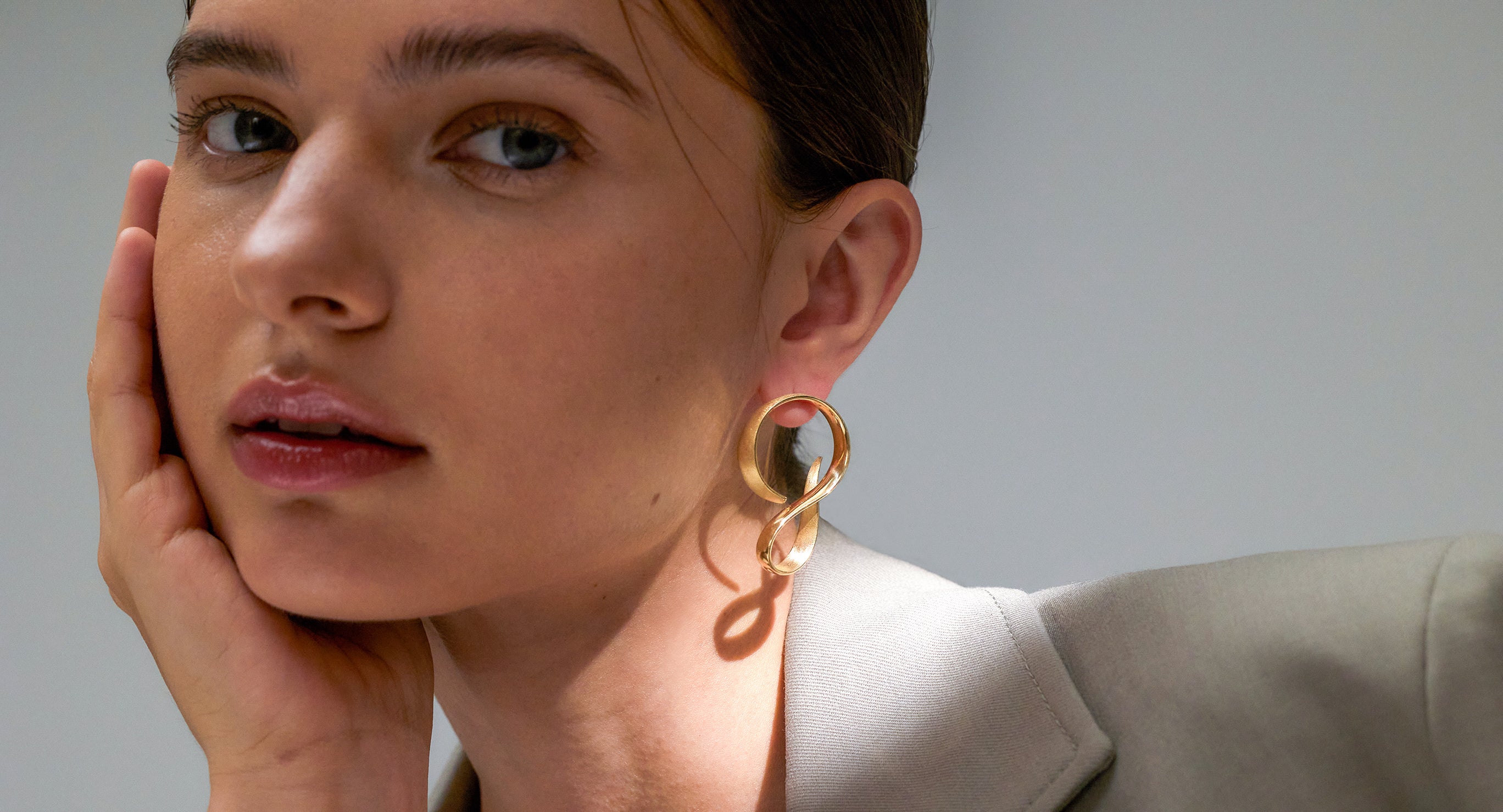 Model wears Yellow Gold Earrings while looking at camera and resting her face in her hand