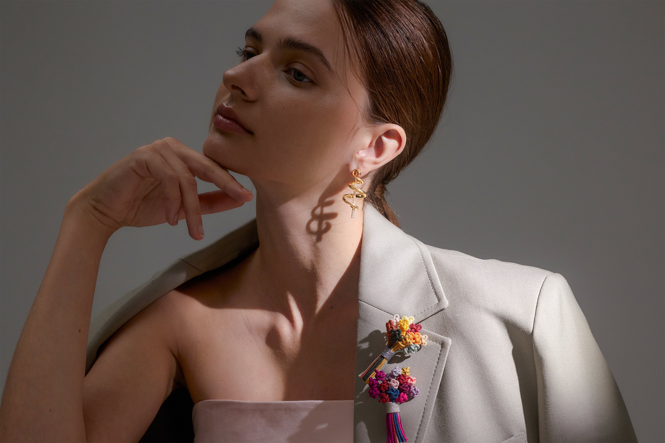 Model wears swirly gold earrings and colorful macrame bouquets on her gray blazer
