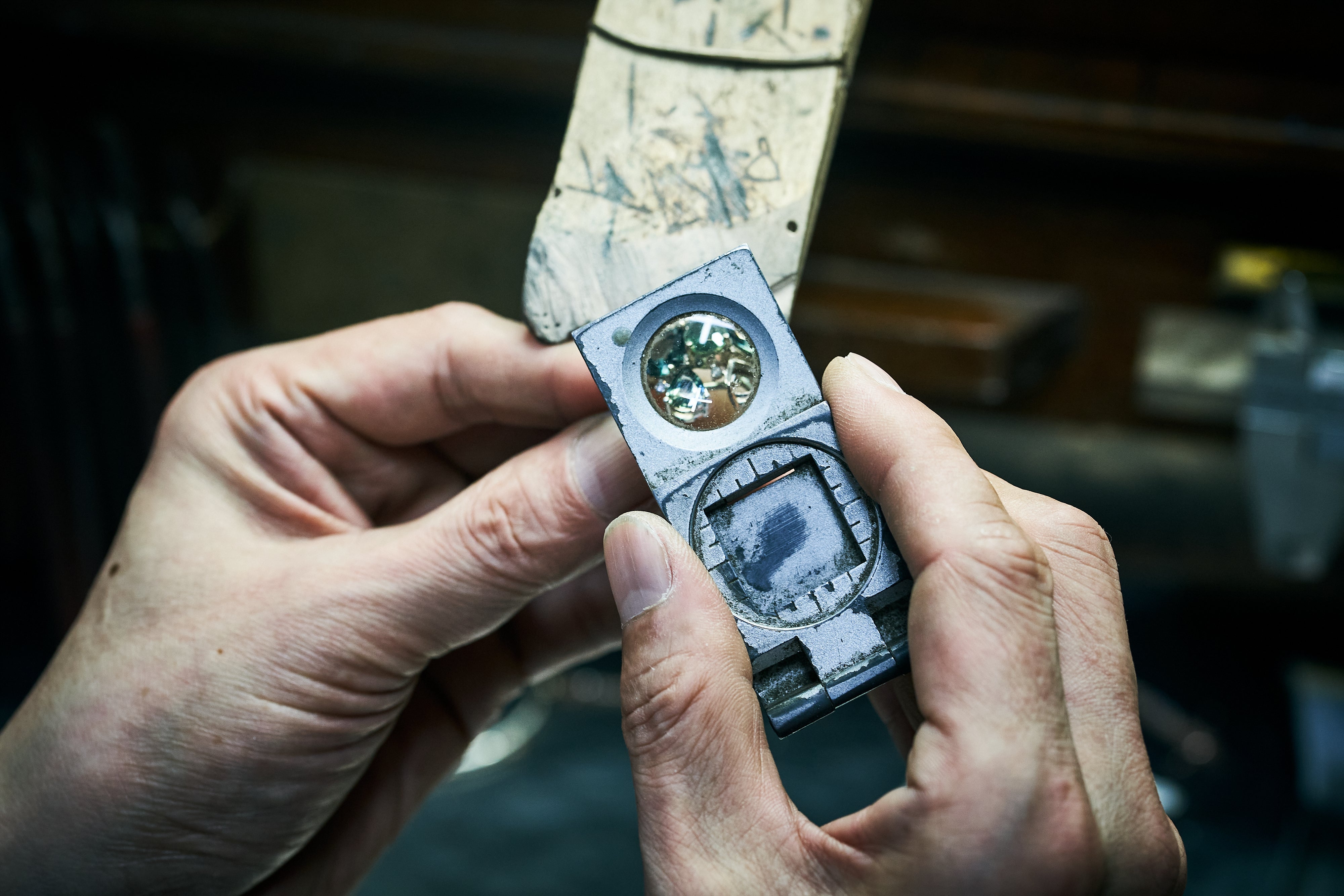 Magnifying glass is used to inspect ring with green gemstones