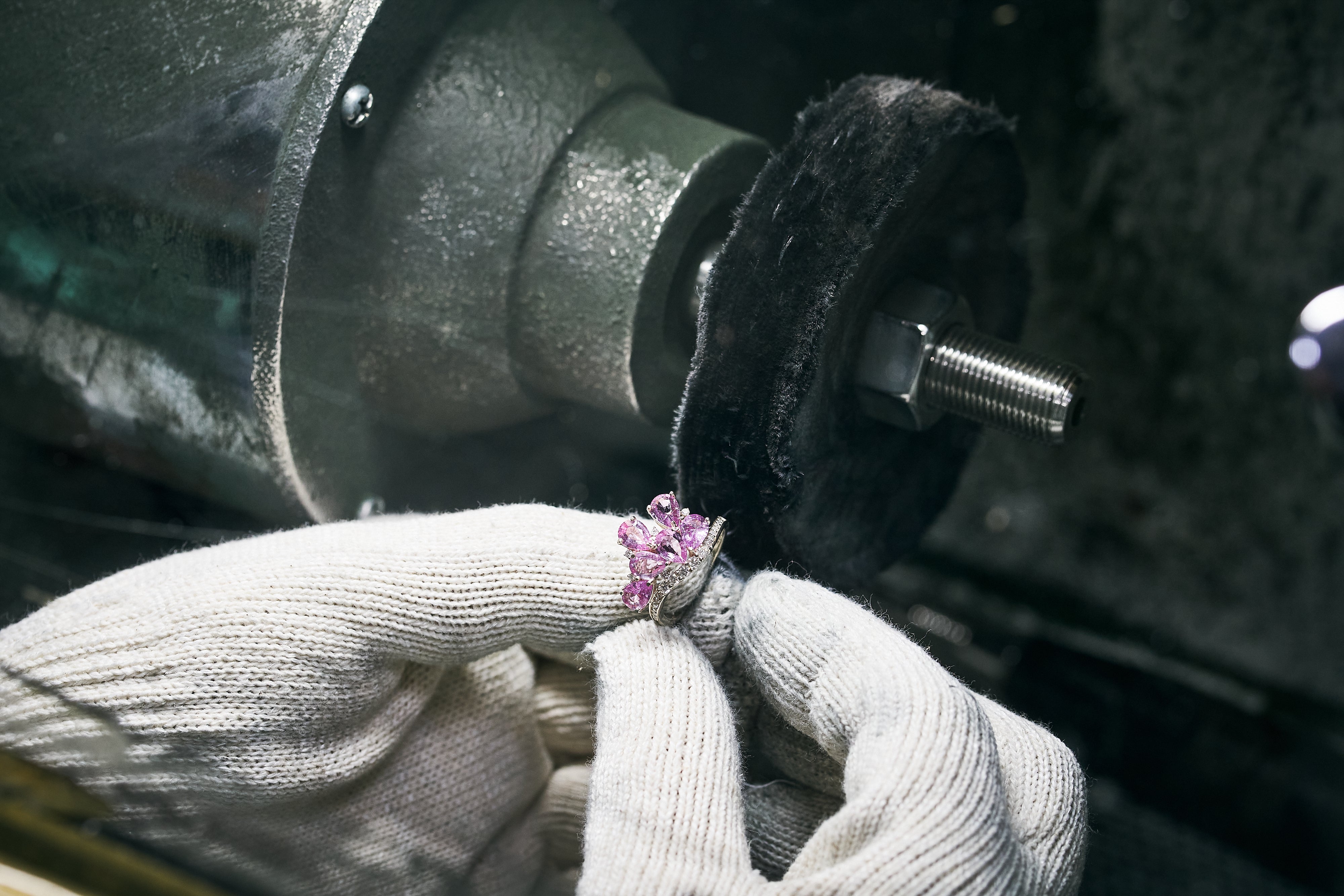 White gold ring with pink gemstones is polished by a buffing wheel